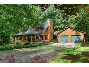 Charming log home with a covered front porch and an attached two-car garage, surrounded by lush greenery and mature trees at 6605 Old White Mill Rd, Fairburn, GA 30213