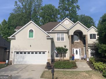 Charming stucco home featuring a two-car garage and a beautifully landscaped front yard with mature trees at 209 Legends Trce, Mcdonough, GA 30253