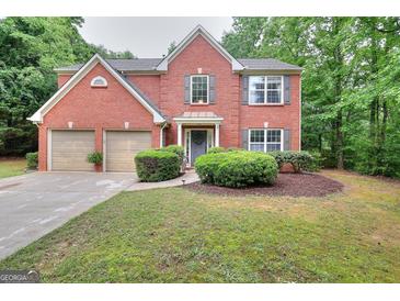 Charming two-story red brick home featuring a manicured lawn and a two-car garage, nestled among mature trees at 5765 Woodstone Dr, Cumming, GA 30028