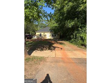 Cozy single-story home with yellow siding, set amongst mature trees and a brick-paved driveway at 908 Emory St, Oxford, GA 30054