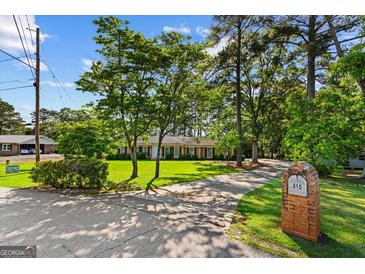 Charming ranch home with mature trees, lush lawn, and a long driveway leading to the house at 315 Burke Cir, Mcdonough, GA 30253