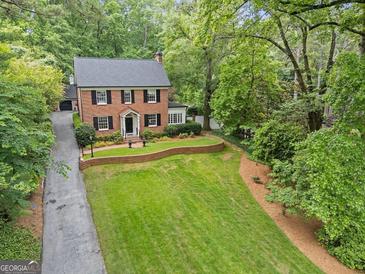 Charming two-story brick home with manicured lawn, brick retaining wall, and mature trees, nestled in a lush, green landscape at 905 Stovall Ne Blvd, Atlanta, GA 30319
