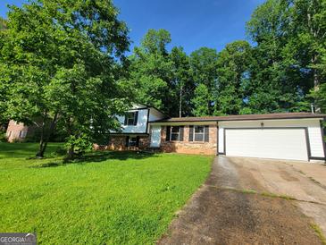 Charming two-story home with brick accents, attached garage, and a lush green lawn surrounded by mature trees at 7290 Grayson Dr, Riverdale, GA 30296