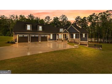 Beautiful exterior of home with large driveway and three-car garage, with a colorful sunset in the background at 180 Lapis Lake Pt, Fayetteville, GA 30215