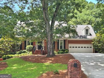 Traditional red brick home featuring a manicured lawn and a two-car garage nestled among mature trees at 2010 Pearwood Path, Roswell, GA 30076