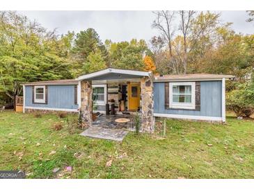 Charming single story home featuring wood facade, stone pillars, yellow door, and a cozy covered porch at 7138 Rockland Rd, Lithonia, GA 30038