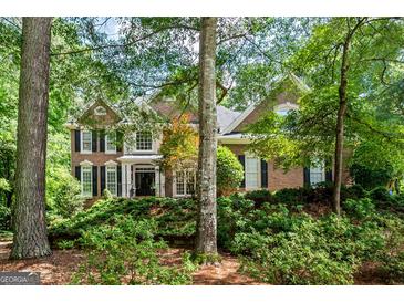 Traditional brick home featuring dark shutters, manicured landscaping and mature trees on a sunny day at 120 Oak Shadow Way, Fayetteville, GA 30215