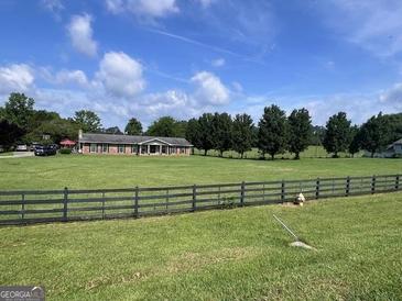 Sprawling front yard with a charming ranch-style home and a classic black wooden fence enhancing the curb appeal at 12621 Highway 142, Oxford, GA 30054