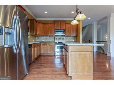Bright kitchen with hardwood floors, stainless steel refrigerator, kitchen island, and natural wood cabinetry at 275 Autry Mill Ln, Suwanee, GA 30024