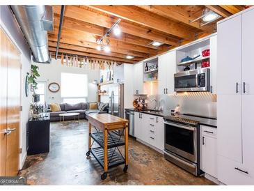 Modern kitchen featuring stainless steel appliances and wooden beams, seamlessly flowing into the living area at 1661 La France Street Ne Unit #216, Atlanta, GA 30307