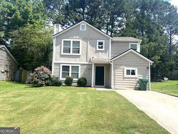 Charming two-story home featuring light beige paint, a well-manicured lawn, and beautiful landscaping at 6300 Creekford Ln, Lithonia, GA 30058