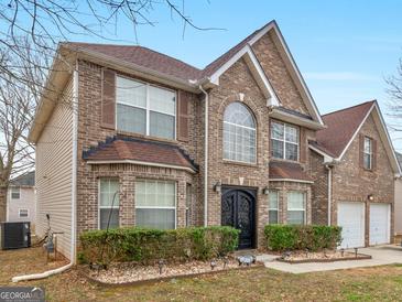 Charming brick two-story home with an attached two-car garage, manicured shrubs, and an arched front entry at 424 Browning Field Way, Hampton, GA 30228