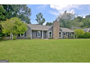 Charming single-story home with a stone chimney, complemented by a lush green lawn and mature trees at 110 Chesterfield Ct, Fayetteville, GA 30214