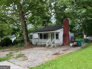 Charming single-story home featuring a cozy porch, brick chimney, and mature trees in a tranquil setting at 766 Warren Dr, Riverdale, GA 30296