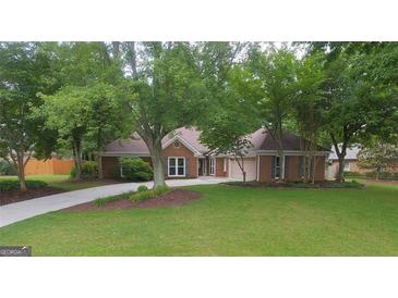 Beautifully landscaped front yard with lush grass and mature trees framing the brick home and driveway at 11940 Wexford Club Dr, Roswell, GA 30075