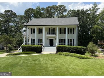 Stately two-story home featuring white siding, black shutters, a well-manicured lawn, and lush landscaping at 107 Edgewater Way, Peachtree City, GA 30269
