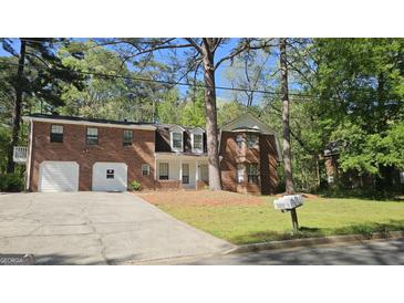 Brick home featuring an attached two-car garage and mature trees in a lush, green landscaped front yard at 2498 Robinhood Dr, Ellenwood, GA 30294