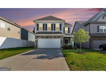 Two-story home featuring stone accents, a two-car garage, a green lawn, and neutral colored siding at 2384 Hastings Manor Ln, Hampton, GA 30228