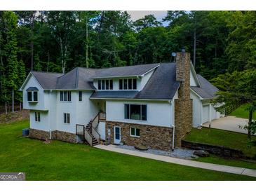 An exterior shot of a home with a stone chimney and front facade with lush green lawn and mature trees at 360 Darren Dr, Fayetteville, GA 30215