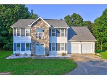 Charming two-story home featuring stone accents, blue shutters, a three-car garage, and a well-maintained front yard at 1067 Misty Meadows Pt, Hampton, GA 30228