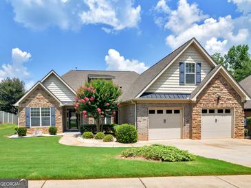 Charming brick and siding home featuring a manicured lawn, blossoming trees, and a two-car garage at 409 Brandy Ln, Mcdonough, GA 30253