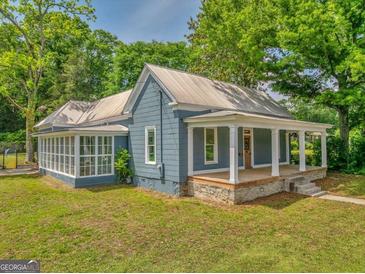 Charming blue home featuring a metal roof, inviting front porch, and a bright sunroom at 1128 Milstead Ne Ave, Conyers, GA 30012