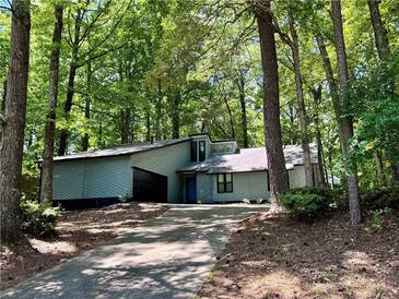 Ranch home with gray siding and a long driveway, nestled among lush trees at 5432 Post Road Pass, Stone Mountain, GA 30088