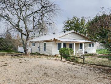 Quaint one-story home featuring neutral siding, metal roof, and a gravel driveway with mature trees in the front yard at 76 Townsend Teague Ne Rd, Fairmount, GA 30139