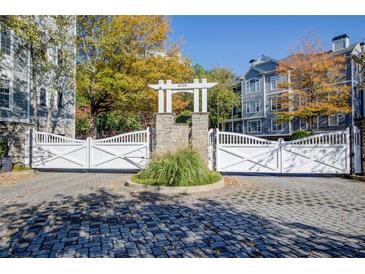 Community entrance featuring white gates, stone pillars, well-maintained landscaping, and cobblestone drive at 4100 Paces Se Walk # 1306, Atlanta, GA 30339