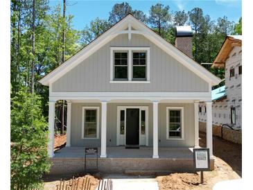 Charming exterior showcasing a covered front porch with columns, a gray facade, and a brick chimney, nestled amongst lush trees at 11792 Serenbe Ln, Chattahoochee Hills, GA 30268