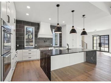 A spacious white kitchen with modern appliances, dark stone countertops, and three pendant lights above the island at 120 Thome Dr, Alpharetta, GA 30022