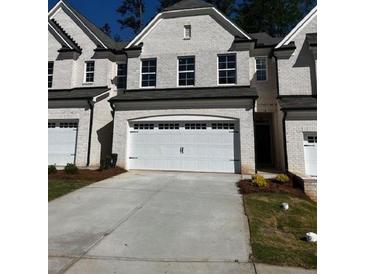 Townhome features a two-car garage and a white brick facade with black trim and a well-maintained lawn at 4150 Cavalier Way, Duluth, GA 30097