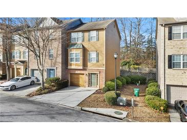 Tan three-story townhome with a brick facade, attached garage, and landscaping at 2793 Keystone Ave, Lithonia, GA 30058