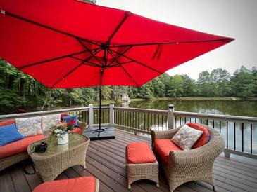 Relaxing deck overlooking a lake, furnished with wicker seating and a red umbrella at 897 Winding Trl, Lawrenceville, GA 30046