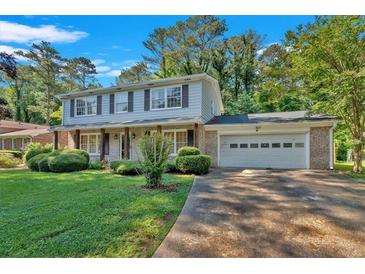 Two-story home with a brick facade, two-car garage, shutters, and lush green lawn and mature landscaping at 1354 Drayton Woods Dr, Tucker, GA 30084