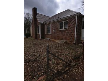 Side view of brick house with a metal roof and windows with bars, fenced-in yard with leaves at 1643 Westhaven Sw Dr, Atlanta, GA 30311