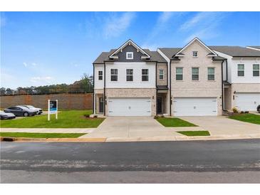 Two-story townhome with white and brick exterior, two-car garage, and landscaped lawn at 8194 Tiger Way, Riverdale, GA 30296