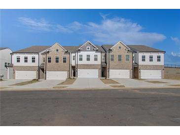 Three-unit townhome building with brick and white siding, two-car garages, and landscaping at 867 Eagle Avenue, Riverdale, GA 30247