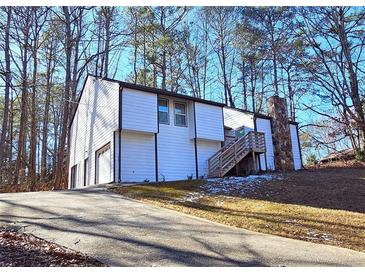 White two-story house with a stone chimney and attached garage, nestled in a wooded setting at 4485 Spring Valley Pkwy, Atlanta, GA 30349