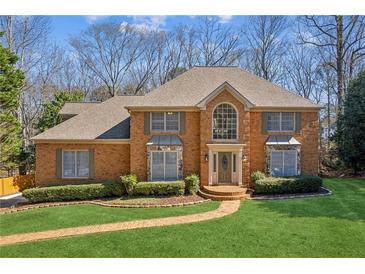 Traditional brick home with manicured lawn and garden beds leading to a front door with decorative glass and sidelights at 3611 Howell Wood Trl, Duluth, GA 30096