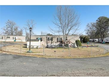 Tan mobile home with a fenced yard, shed, and landscaping at 127 Cambridge Ct, Hampton, GA 30228