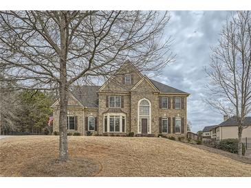 Brick two-story house with shutters, a large front yard, and mature trees at 6620 Flagstone Mill Cv, Cumming, GA 30028