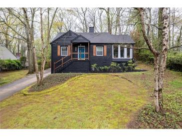 Charming, two-story home featuring a black exterior, brick chimney, and front yard with mature trees at 2597 Elsinore St, East Point, GA 30344