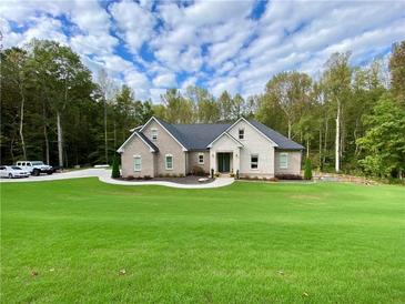 Brick house with large green lawn, driveway, and wooded area in background at 5710 Breitling Dr, Cumming, GA 30028