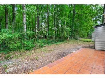 A spacious backyard with a tile patio surrounded by lush trees and greenery offers privacy and outdoor living at 1428 Muirfield Dr, Stone Mountain, GA 30088