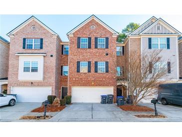 View of the brick townhome exterior with black shutters, a two car garage, landscaping, and a front door at 1605 Signal Flag Way, Lawrenceville, GA 30043