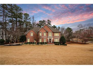 Two-story brick home featuring a manicured lawn and complemented by mature trees under a colorful sunset sky at 5216 Old Mountain Ln, Powder Springs, GA 30127
