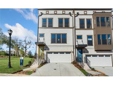 View of a modern townhome featuring a two-car garage, neutral color palette, and a well-manicured lawn at 1119 Rivard Nw Cir, Atlanta, GA 30318