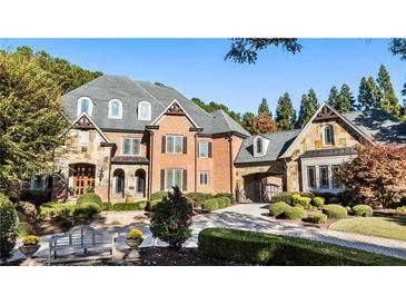 Elegant brick home with stone accents, lush landscaping, and a circular driveway, creating a welcoming and luxurious curb appeal at 1050 Carnoustie Ln, Alpharetta, GA 30005