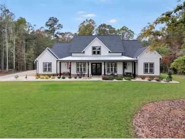 Stunning modern farmhouse featuring a covered front porch, black trim windows, and a lush green lawn at 3911 Peeksville Rd, Locust Grove, GA 30248